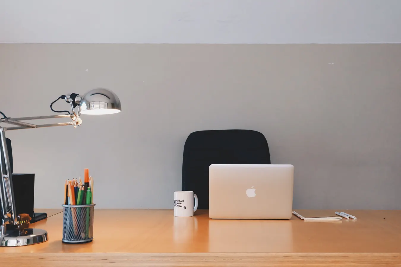 Minimal office desk with a laptop, desk lamp, chair, and cup of colored pencils